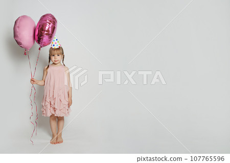 Cheerful child holding two pink balloon on white studio wall banner background.  107765596