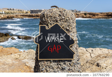 Wage gap symbol. Concept words Wage gap on wooden blocks on a beautiful black chalk blackboard on a beautiful beach stone blue sea background. Business, support and wage gap concept. Copy space. 107768290