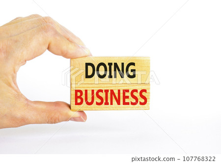 Doing business symbol. Concept words Doing business on beautiful wooden block. Beautiful white table white background. Businessman hand. Business, motivational Doing business concept. Copy space. Doing business symbol. Concept words Doing business on beautiful wooden block. Beautiful white table white background. Businessman hand. Business, motivational Doing business concept. Copy space. 107768322