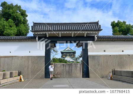 Walking around Osaka Castle in early autumn, the castle tower seen beyond the cherry blossom gate Walking around Osaka Castle in early autumn, the castle tower seen beyond the cherry blossom gate 107768415