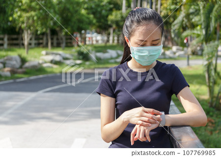 young asian woman in medical protective mask doing setting smart watch application before exercise in the morning.working out outdoor. Concept of healthy young asian woman in medical protective mask doing setting smart watch application before exercise in the morning.working out outdoor. Concept of healthy 107769985