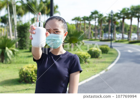 Young woman in medical protective mask and holding an alcohol in hand. campaign to use protective mask and alcohol  for protect COVID19 107769994