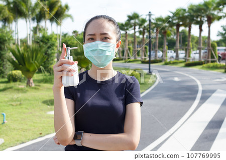 Young woman in medical protective mask and holding an alcohol in hand. campaign to use protective mask and alcohol for protect COVID19 Young woman in medical protective mask and holding an alcohol in hand. campaign to use protective mask and alcohol for protect COVID19 107769995