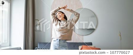 Joyful young korean woman dancing, raising hands up and looking upbeat, feeling healthy and upbeat Joyful young korean woman dancing, raising hands up and looking upbeat, feeling healthy and upbeat 107770027