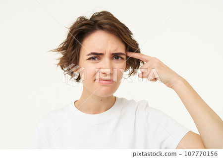 Young woman rolling finger on forehead and looking with disappointment, thinks someone is stupid or crazy, isolated over white background Young woman rolling finger on forehead and looking with disappointment, thinks someone is stupid or crazy, isolated over white background 107770156