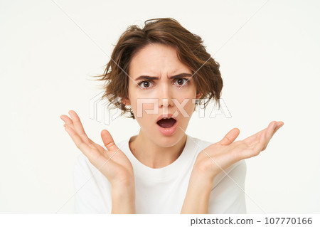 Close up of shocked brunette woman, shrugging and looking disappointed, posing over white studio background 107770166