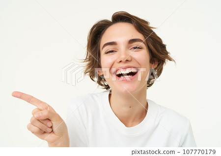 Image of candid brunette girl, pointing left, showing advertisement, recommending store, standing over white background 107770179