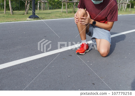 Sport man in medical protective mask suffering with pain on sports running knee injury after running.Injury from workout concept 107770258