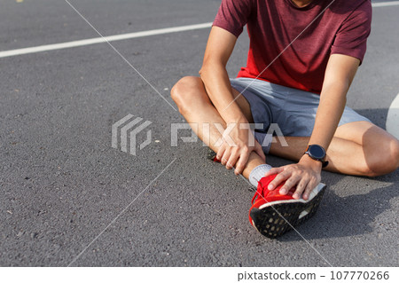 Sport man holding ankle in pain due to sprained ankle. Injury from workout concept 107770266