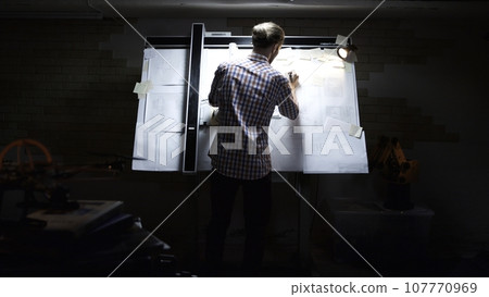Rear view of male architect working on blueprint. Rear view of engineer drawing project of business district. Rear view of man engineer drawing Rear view of male architect working on blueprint. Rear view of engineer drawing project of business district. Rear view of man engineer drawing 107770969