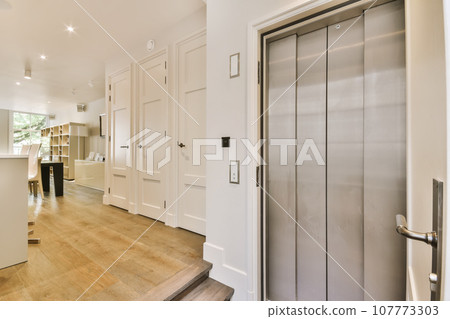 a kitchen and living room in a house with white walls, hardwood flooring and stainless steel door handles on the doors 107773303