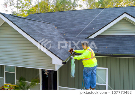 Worker is cleaning clogged roof gutter from dirt, debris fallen leaves to prevent water let rainwater drain Worker is cleaning clogged roof gutter from dirt, debris fallen leaves to prevent water let rainwater drain 107773492