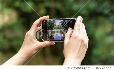 Hands holding smartphone, taking mobile photo, capturing nature, forest and lake Hands holding smartphone, taking mobile photo, capturing nature, forest and lake 107776366