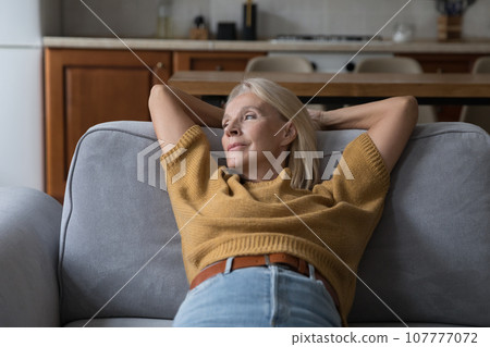 Relaxed peaceful middle aged 50s woman resting on comfortable couch 107777072