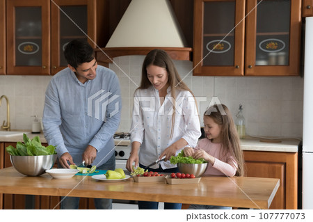 Cheerful parents and cute kid girl cooking salad together 107777073