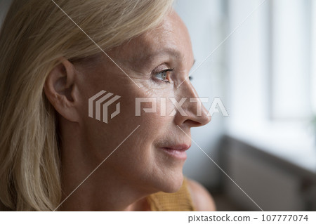 Face of blonde senior mature woman looking at window away 107777074