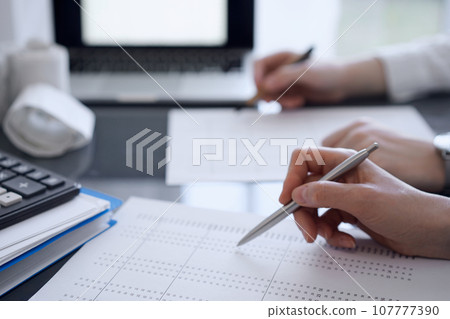 Two accountants use a calculator and tablet computer for counting taxes or revenue balance. Business, audit, and taxes concepts 107777390