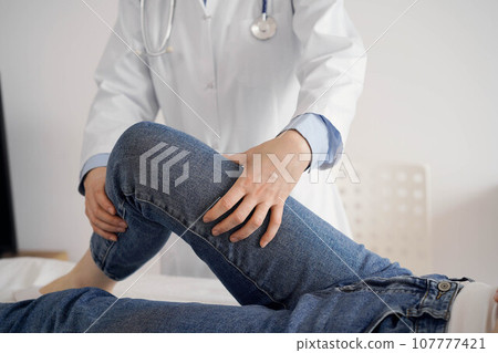 Doctor and patient are at the usual medical inspection in the clinic. Therapist examines a young woman's knee. Medicine concept Doctor and patient are at the usual medical inspection in the clinic. Therapist examines a young woman's knee. Medicine concept 107777421