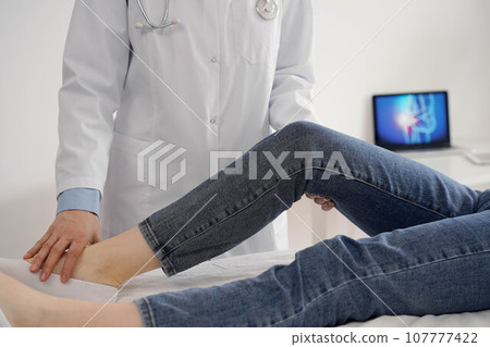 Doctor and patient are at the usual medical inspection in the clinic. Therapist examines a young woman's knee. Medicine concept 107777422