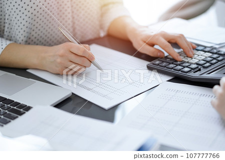 Woman accountant using a calculator and laptop computer while counting taxes with a client or a colleague. Business audit team, finance advisor 107777766