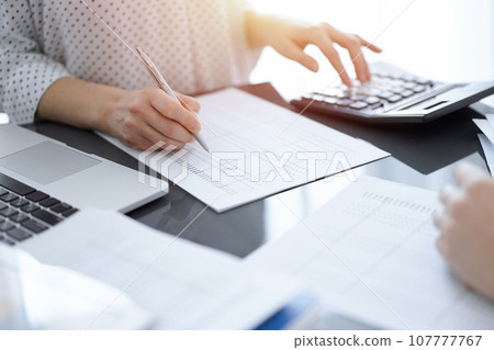 Woman accountant using a calculator and laptop computer while counting taxes with a client or a colleague. Business audit team, finance advisor Woman accountant using a calculator and laptop computer while counting taxes with a client or a colleague. Business audit team, finance advisor 107777767