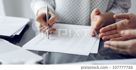 Woman accountant using a calculator and laptop computer while counting and discussing taxes with a client. Business audit and finance concepts 107777788