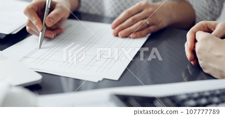 Woman accountant using a calculator and laptop computer while counting taxes for a client. Business audit and finance concepts 107777789