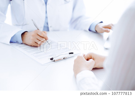 Doctor and patient discussing something and using laptop while sitting opposite each other at the desk in clinic office. Perfect medical service and medicine concept Doctor and patient discussing something and using laptop while sitting opposite each other at the desk in clinic office. Perfect medical service and medicine concept 107777813