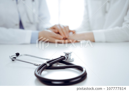 Stethoscope lying on the tablet computer in front of a doctor and patient sitting near each other. Medicine, reassuring hands concept 107777814