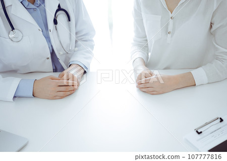 Doctor and patient sitting near of each other at the table in clinic, closeup. Medicine concept Doctor and patient sitting near of each other at the table in clinic, closeup. Medicine concept 107777816