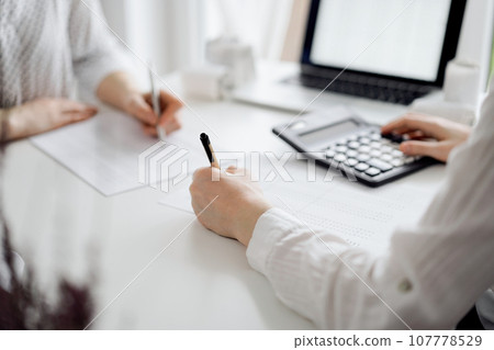 Two accountants using a laptop computer and calculator for counting taxes at white desk in office. Teamwork in business audit and finance 107778529