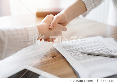 Business people shaking hands above contract papers just signed on the wooden table, close up. Lawyers at meeting. Teamwork, partnership, success concept 107778550