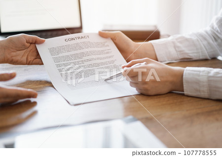 Businesswoman lawyer pointing into contract special points admitting something for colleague or client at the wooden desk in office. Business people teamwork and partnership, meeting concept 107778555