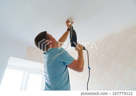 A man is working on the installation of a ceiling luminaire on the ceiling. A man is working on the installation of a ceiling luminaire on the ceiling. 107779122