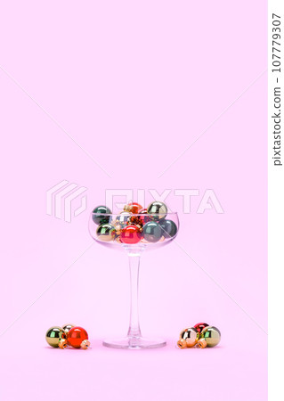 Cocktail glass and Christmas decorations on pastel pink background. Minimal Creative Christmas concept. Gold, green and red Christmas baubles in a cocktail glass and around. Happy New Year shot. 107779307