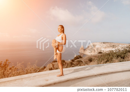 Fitness woman sea. A happy middle aged woman in white sportswear exercises morning outdoors in a park with a beach view. Female fitness pilates yoga routine concept. Healthy lifestyle. Fitness woman sea. A happy middle aged woman in white sportswear exercises morning outdoors in a park with a beach view. Female fitness pilates yoga routine concept. Healthy lifestyle. 107782011