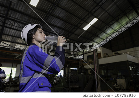 Women engineer drinking water from plastic bottle after working at factory during break. Women engineer drinking water from plastic bottle after working at factory during break. 107782936
