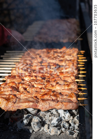A lot of juicy meat kebabs in a row on the grill. Meat pieces strung on wooden skewers on the grill. The process of cooking kebabs with a lot of smoke. Cooking in nature 107783635