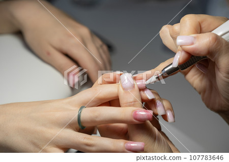 Female hands and tools for manicure, process of performing manicure in beauty salon. Nail care procedure in a beauty salon. Gloved hands of a skilled manicurist cutting cuticles. Concept spa body care Female hands and tools for manicure, process of performing manicure in beauty salon. Nail care procedure in a beauty salon. Gloved hands of a skilled manicurist cutting cuticles. Concept spa body care 107783646