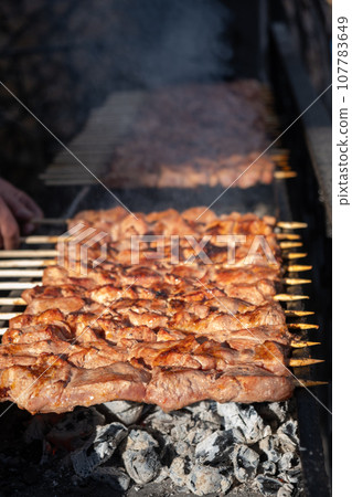 A lot of juicy meat kebabs in a row on the grill. Meat pieces strung on wooden skewers on the grill. The process of cooking kebabs with a lot of smoke. Cooking in nature A lot of juicy meat kebabs in a row on the grill. Meat pieces strung on wooden skewers on the grill. The process of cooking kebabs with a lot of smoke. Cooking in nature 107783649