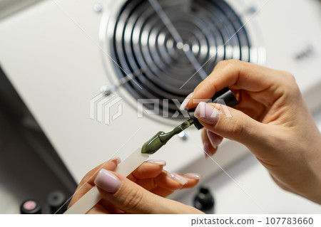 A manicurist applies gel nail polish to empty tips as a sample for future clients. Large range of gel polishes. Spa body care concept. Nail technician A manicurist applies gel nail polish to empty tips as a sample for future clients. Large range of gel polishes. Spa body care concept. Nail technician 107783660