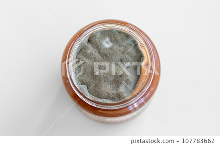 Open jar with sweet jam and mold on a white background. Mold in a jar of raspberry jam. Hazardous to health.  107783662