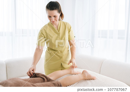 Portrait of pediatric female masseuse massaging calf muscle of unrecognizable teenager girl client lying on massage couch at spa salon. Little pretty kid getting legs massage in medical clinic. Portrait of pediatric female masseuse massaging calf muscle of unrecognizable teenager girl client lying on massage couch at spa salon. Little pretty kid getting legs massage in medical clinic. 107787067