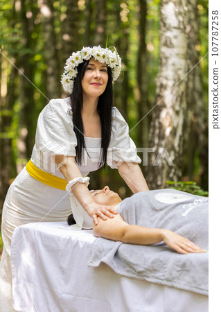 Therapist female doctor making woman relaxing spa face massage with hands outdoors in the forest 107787258
