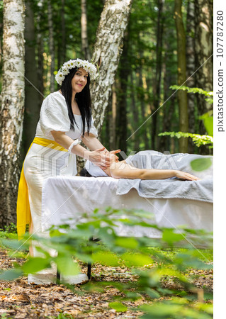 Therapist female doctor making woman relaxing spa face massage with hands outdoors in the forest Therapist female doctor making woman relaxing spa face massage with hands outdoors in the forest 107787280