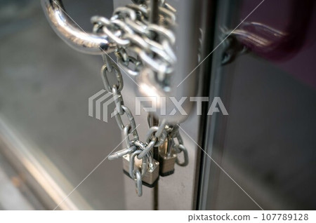 Chain and padlock on closed business glass door with metal handles Chain and padlock on closed business glass door with metal handles 107789128