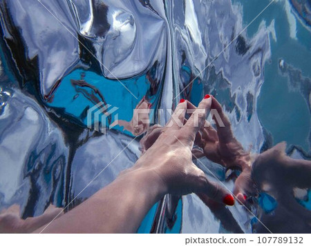 Close up of woman's hand reaching for distorted mirror reflection Close up of woman's hand reaching for distorted mirror reflection 107789132