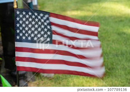 Motion blur fluttering American flag graveside in sunny grass cemetery Motion blur fluttering American flag graveside in sunny grass cemetery 107789136