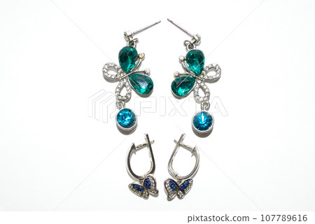 Two pairs of female silver earrings with shiny crystals and butterflies isolated on white background Two pairs of female silver earrings with shiny crystals and butterflies isolated on white background 107789616