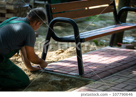 Installation of a park bench for paving stones in a designated place in the city park. 107790646